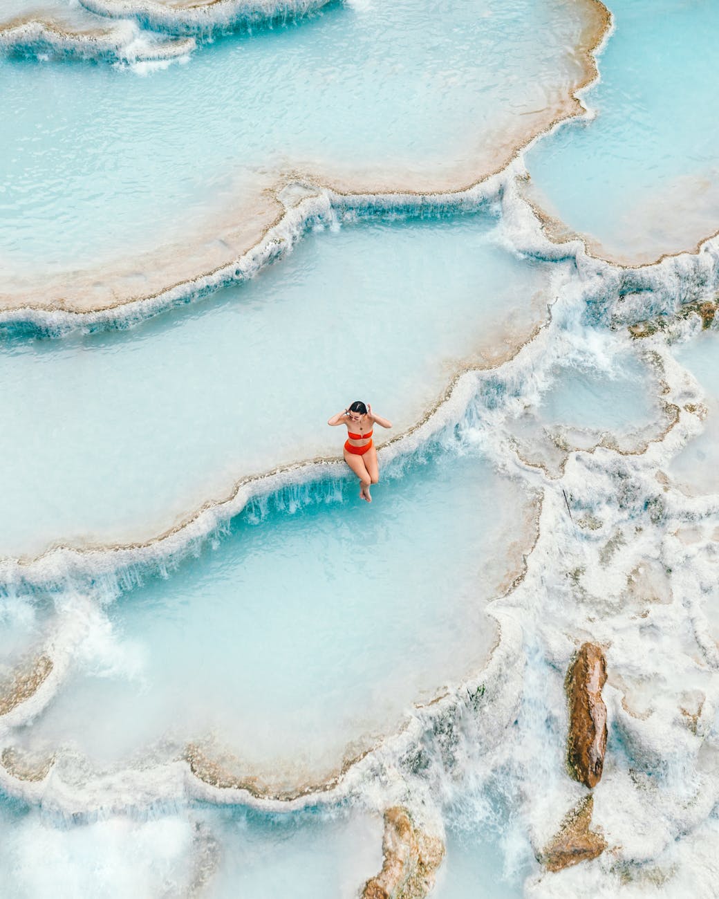 woman in red bikini standing on brown rock formation in front of body of water during