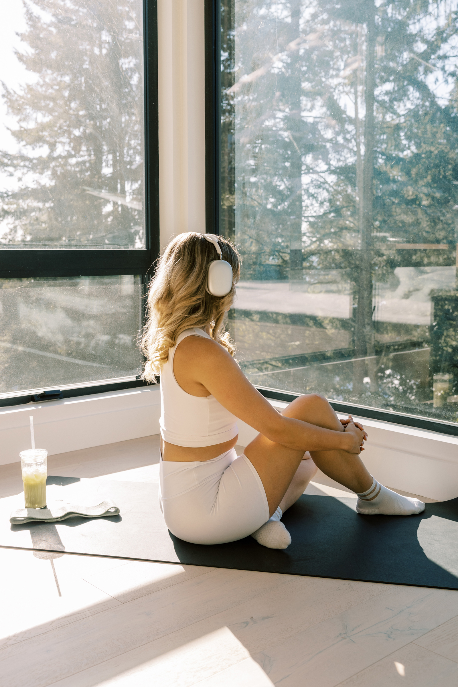 woman in white workout clothes with white headphone stretching and looking out the window