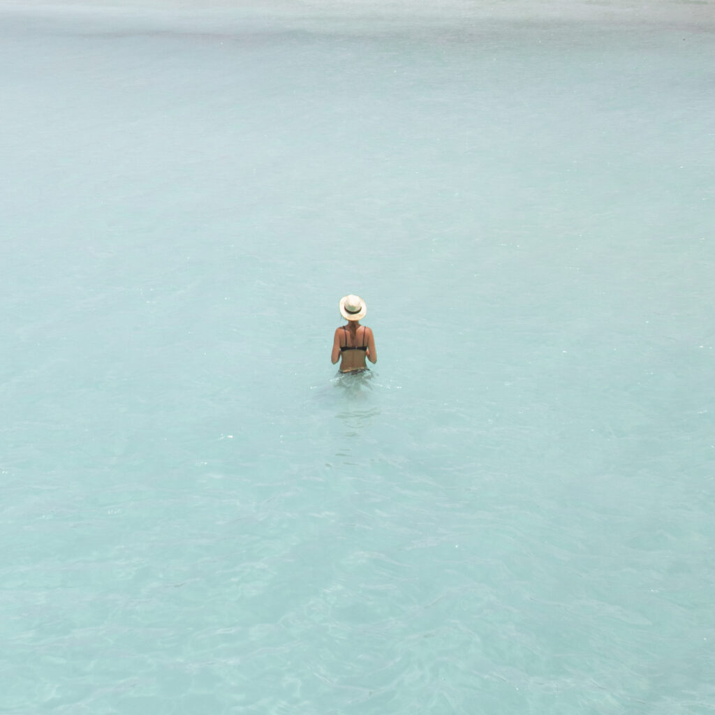 Woman in her early 50s ona. solo trip, standing in blue ocean water